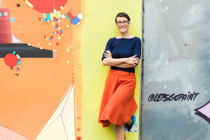 Dawn Smith standing, leaning against a wall covered with creative graffit art
